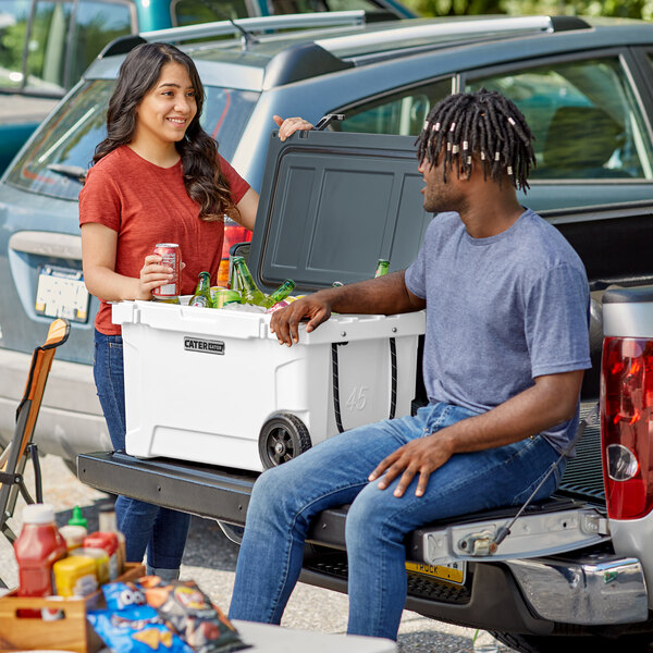 A man and woman sitting in the back of a truck with a CaterGator cooler.