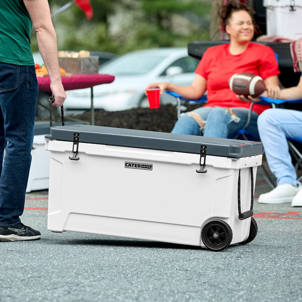 A person pushing a white CaterGator cooler on wheels.