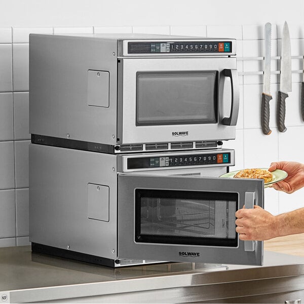 A person holding a plate of food in front of a Solwave commercial microwave.