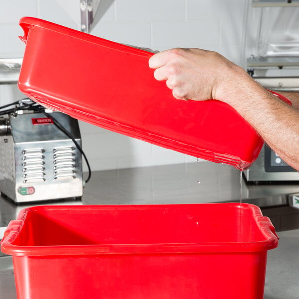 A person pouring liquid into a red Vollrath Color-Mate drain box.