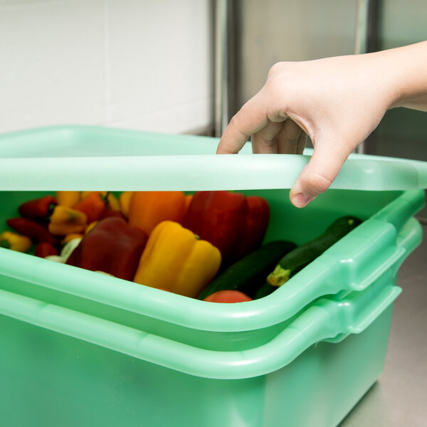 A hand using a Vollrath Traex green lid to cover a container of vegetables.