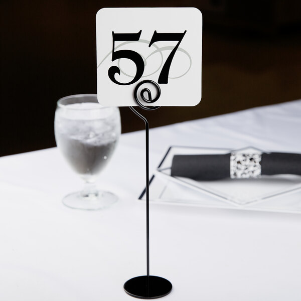 A black iron Cal-Mil table number holder on a stand holding a white table number.