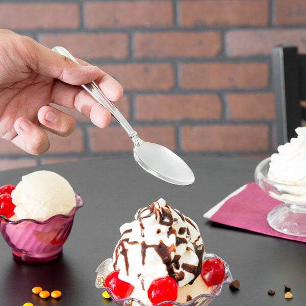 A hand holding a Oneida Unity stainless steel oval bowl spoon over a scoop of ice cream.