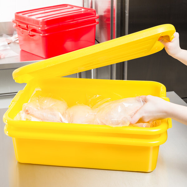 A woman using a Vollrath yellow food storage container to hold a plastic bag of chicken.