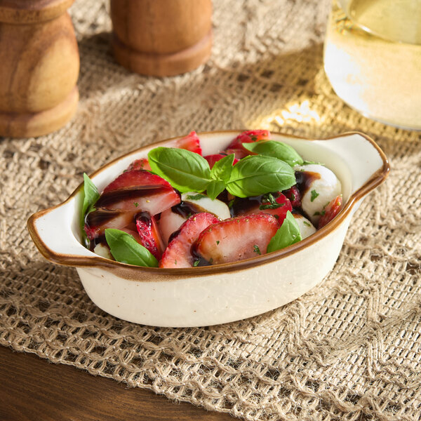 A table with a bowl of fruit salad in a Acopa Keystone porcelain mini rarebit dish.