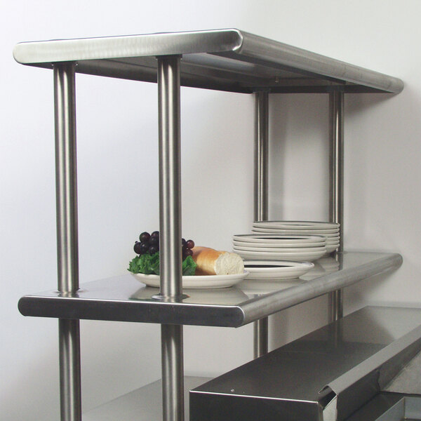A stainless steel Advance Tabco double deck overshelf on a table with plates and food on it.