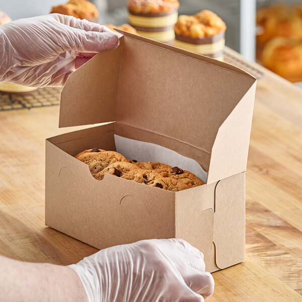 A person in gloves holding a Baker's Lane Kraft cupcake box filled with muffins.