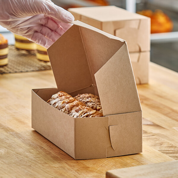 A hand in a white glove taking a loaf of bread out of a cardboard bakery box.