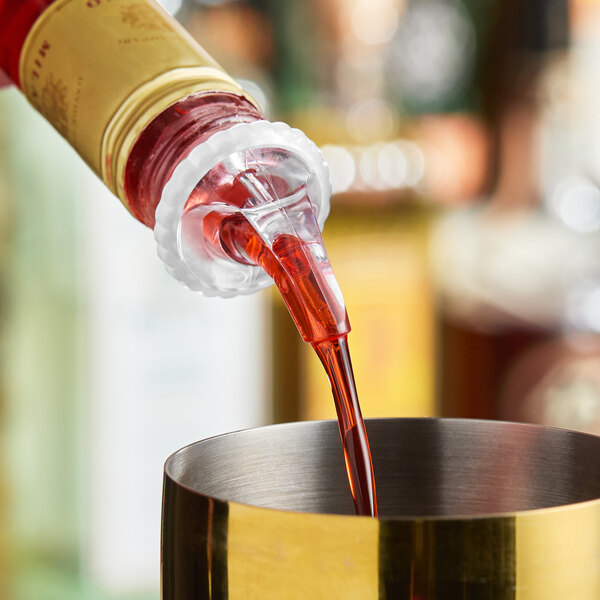 A bottle with a clear measured liquor pourer dispensing red liquid into a metal container.