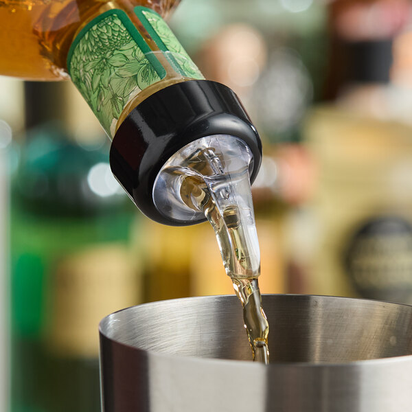 A bottle with an Acopa 1.25 oz. 3-ball measured liquor pourer with collar dispensing liquid into a metal container.