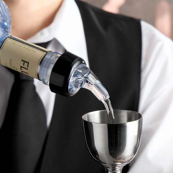 A clear plastic measured liquor pourer with a black collar attached to a bottle, dispensing liquid into a metal jigger.