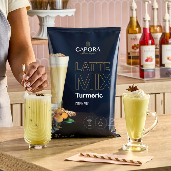 A bag of Capora Turmeric Latte Mix displayed on a counter with two prepared turmeric lattes in glass mugs.