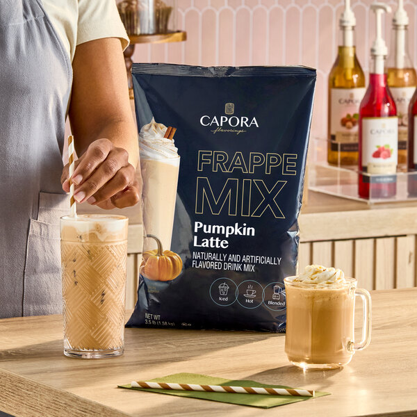 A 3.5 lb. bag of Capora Pumpkin Latte Frappe Mix displayed on a counter with prepared iced and hot pumpkin latte drinks.