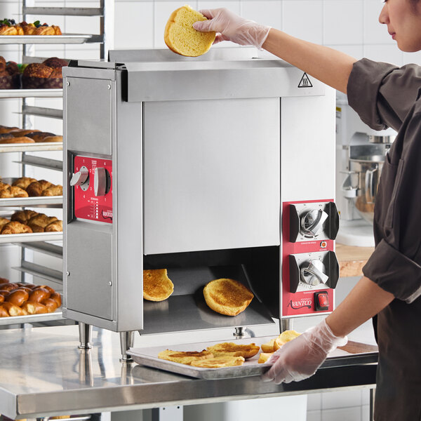 A compact vertical contact bun toaster with stainless steel housing and red control panels, used for toasting buns in a commercial kitchen setting.
