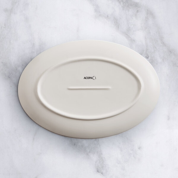 An Acopa Cape white porcelain oval platter with a white rim on a marble surface.