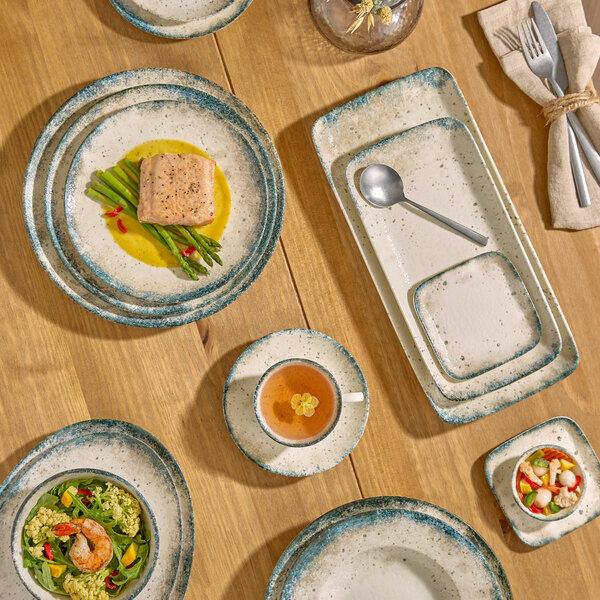 A set of round gray porcelain bowls and plates with a speckled design, arranged on a wooden table with food and utensils.