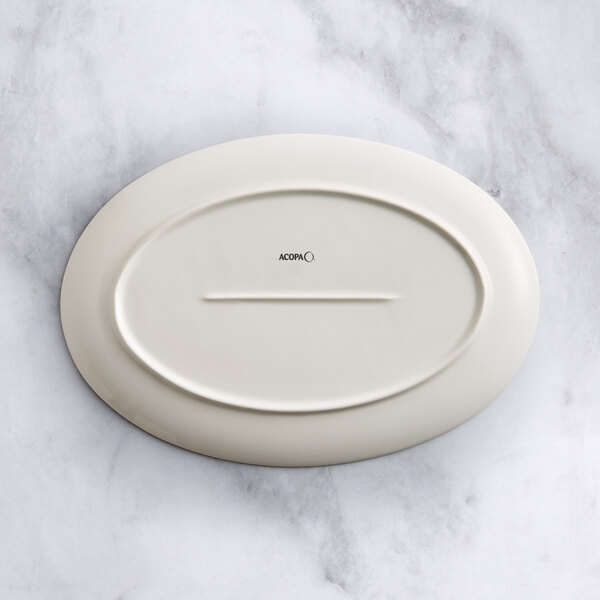 An Acopa Cape beige oval porcelain platter on a marble surface.