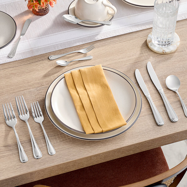 A table with a white plate, napkins, and Acopa Edgeworth stainless steel spoons.