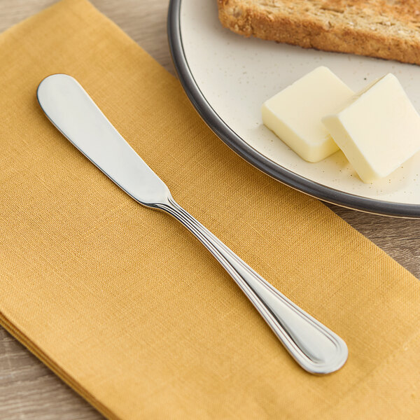 An Acopa stainless steel butter spreader on a napkin next to a piece of bread.
