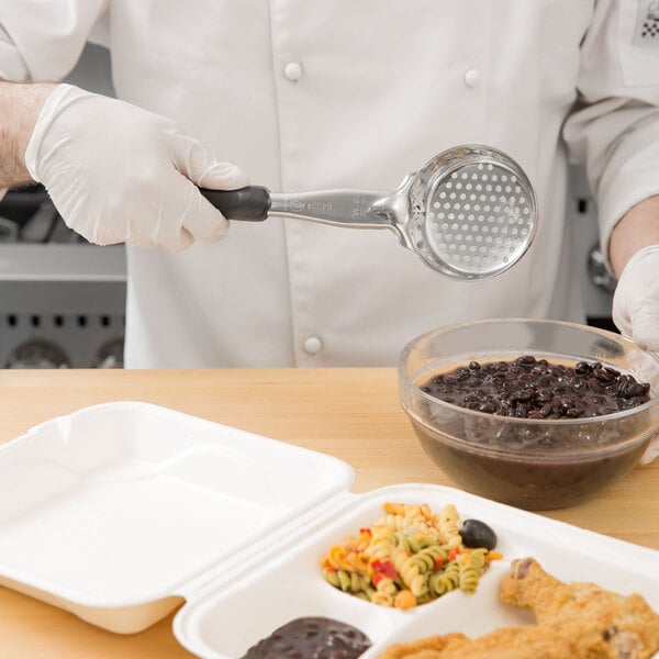 A person using a Vollrath black perforated round Spoodle to serve food from a white container.