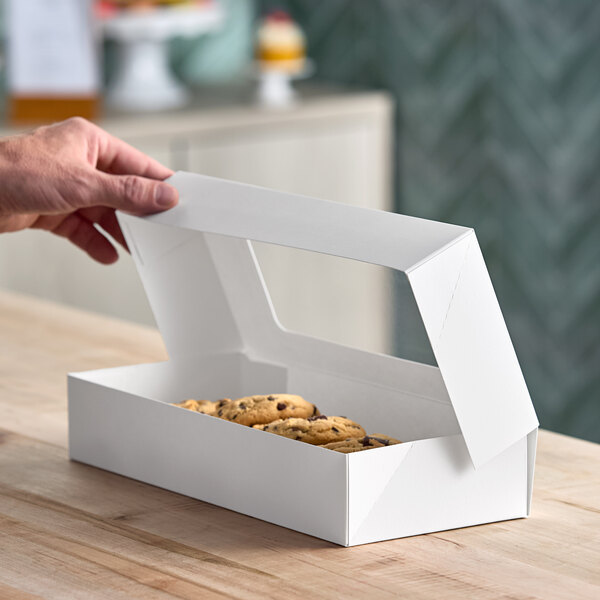 A white rectangular bakery box with a clear window on the lid, partially open to reveal cookies inside.