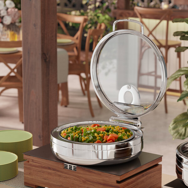 A round stainless steel induction chafer with a glass top and soft close lid, filled with mixed vegetables.