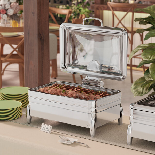 A stainless steel Acopa Manchester chafer stand on a table with food and plates.