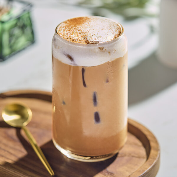 A Acopa Select rim tempered can glass of iced coffee with a spoon on a wooden tray.