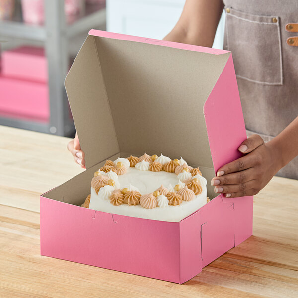 A pink bakery box containing a decorated cake with white and tan frosting.