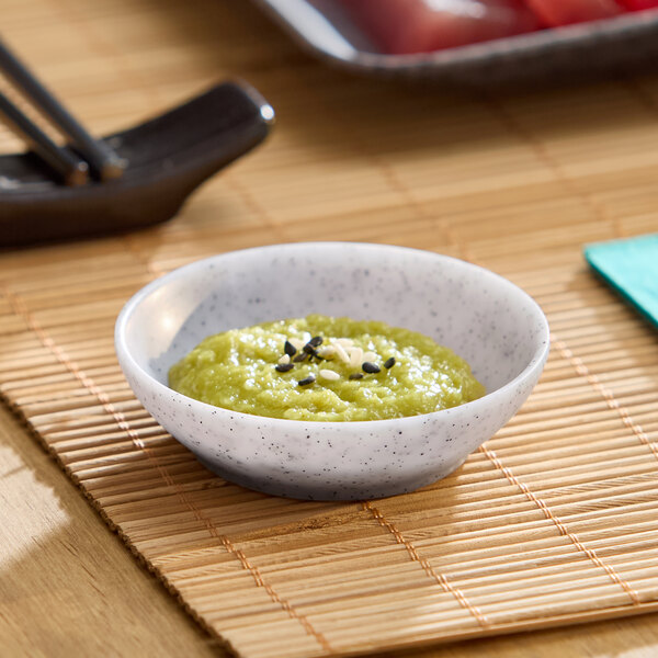 A small light gray round melamine ramekin filled with green paste and garnished with seeds.