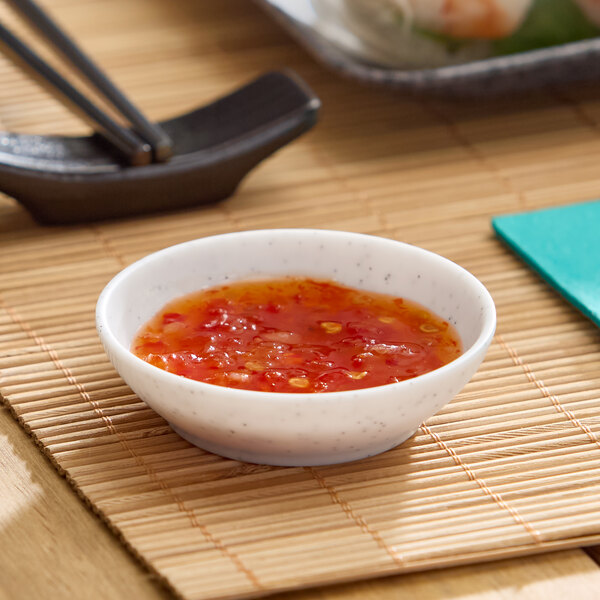 A small white round melamine ramekin filled with a red dipping sauce.