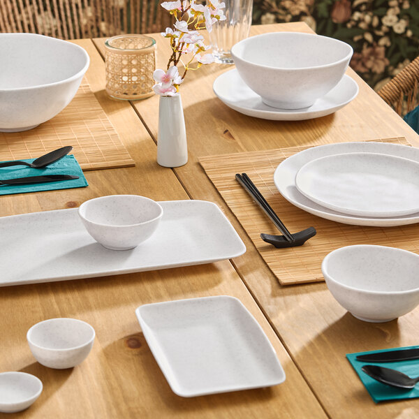 A set of small white round melamine ramekins placed on a wooden dining table with other dinnerware.