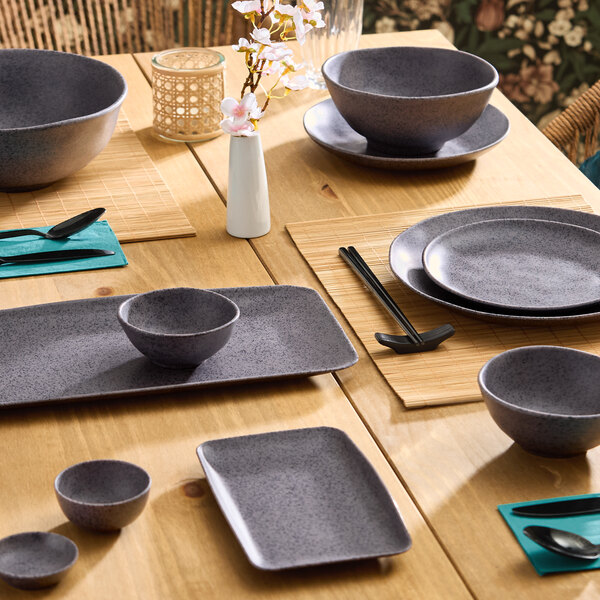 A dark gray rectangular melamine platter displayed on a wooden dining table with matching dinnerware.