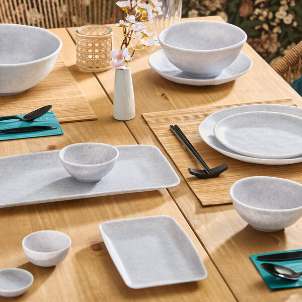 A set of light gray round melamine ramekins placed on a wooden dining table with other matching dinnerware.