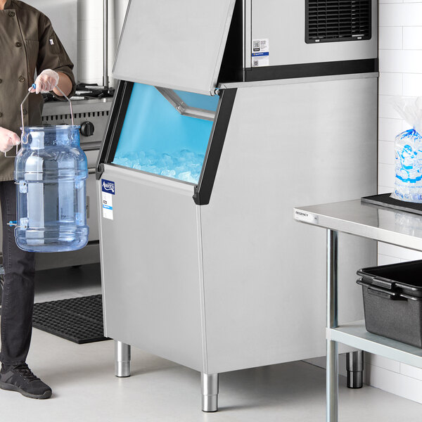 A stainless steel ice storage bin with an open lid, partially filled with ice.