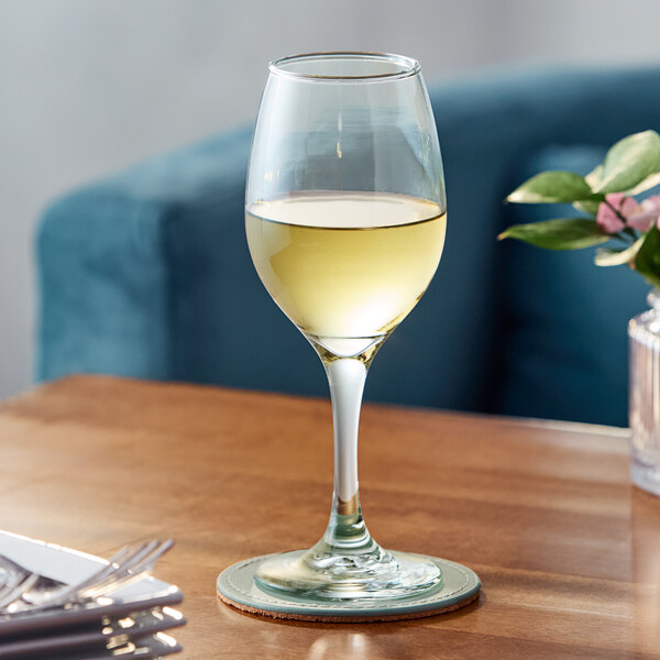 A clear all-purpose wine glass filled with white wine, placed on a wooden table.
