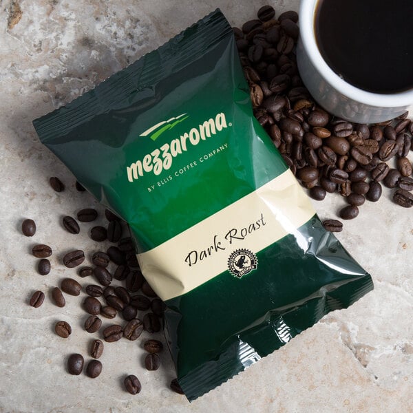 A bag of Ellis Mezzaroma Dark Roast Coffee packets next to a cup of coffee and coffee beans.
