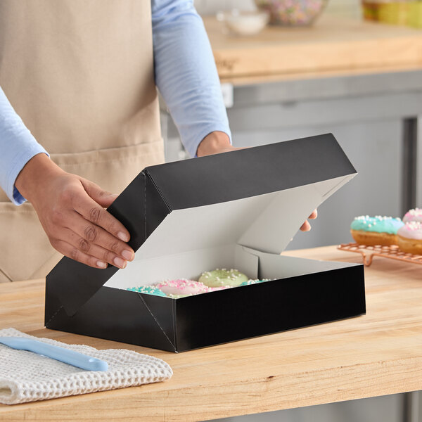 A black auto-popup bakery box being opened, containing donuts inside.