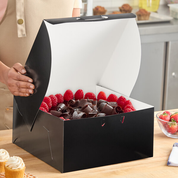 A black 12 x 12 x 6 inch bakery box containing a cake, shown open on a countertop.
