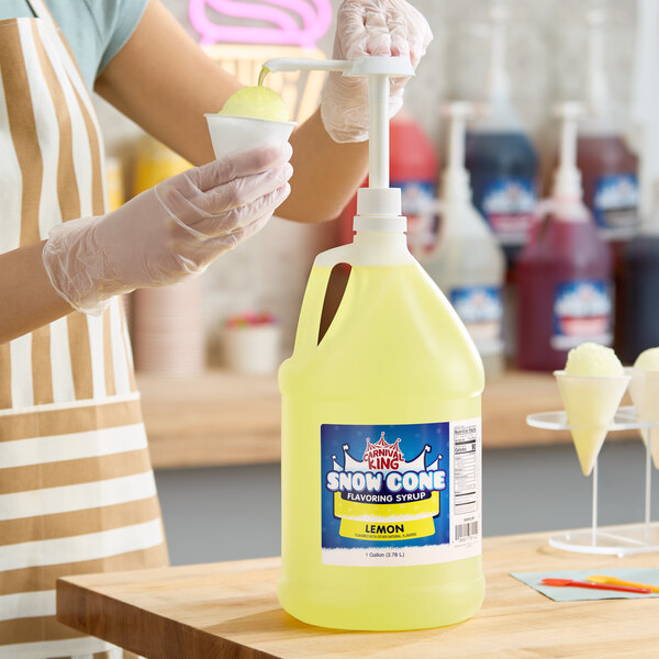 A gallon jug of Carnival King Lemon Snow Cone Flavoring Syrup with a pump dispenser being used to pour syrup onto a snow cone.