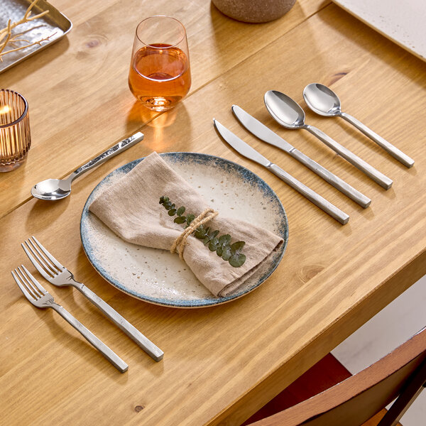 An extra heavy weight stainless steel dinner fork with a modern, squared handle design placed on a wooden dining table.