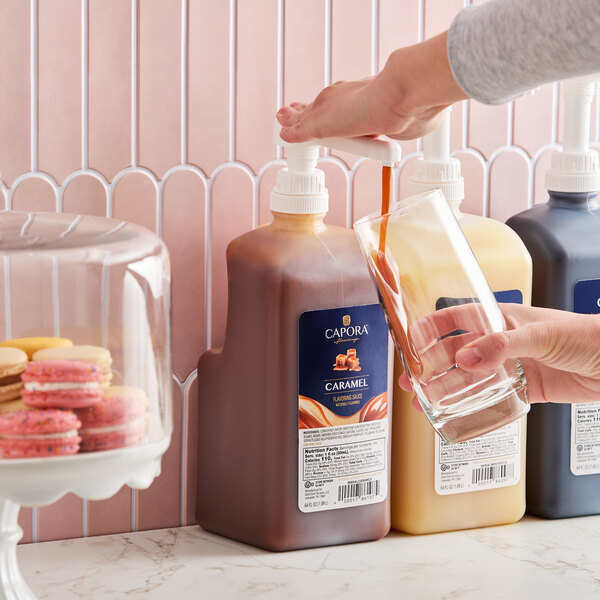 A large pump bottle of Capora Caramel Flavoring Sauce being dispensed into a glass.