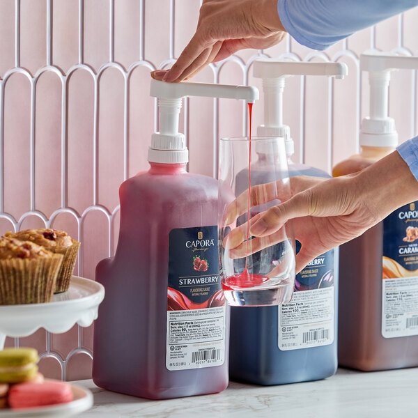 A bottle of Capora Strawberry Flavoring Sauce with a pump dispenser being used to pour sauce into a glass.
