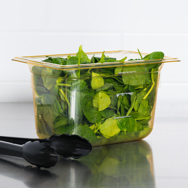 A Vollrath amber plastic food pan with spinach leaves inside.