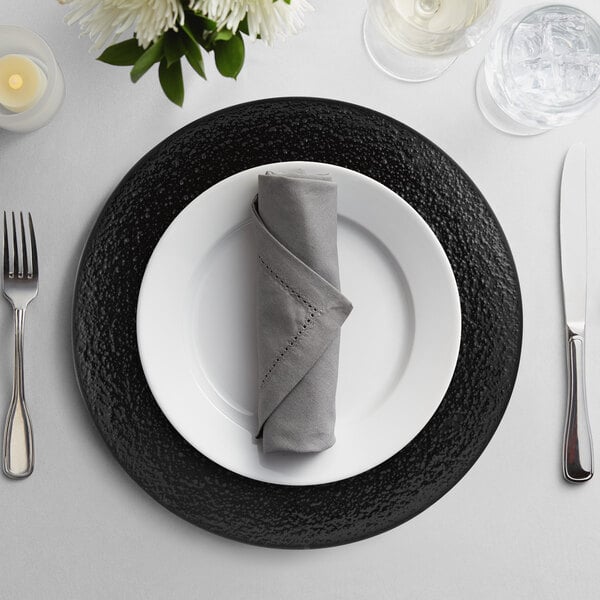 A black 10 Strawberry Street glass charger plate with silverware on a table.