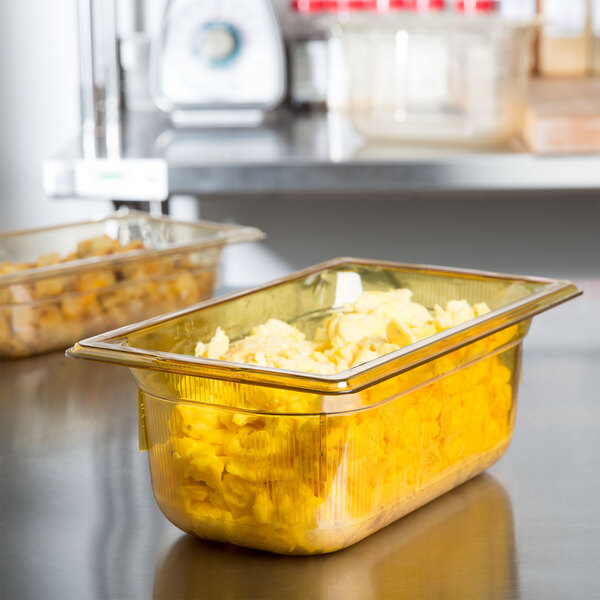 A Vollrath amber plastic food pan filled with yellow food on a counter.