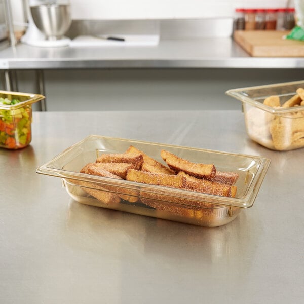 A Vollrath amber plastic food pan on a counter with food in it.