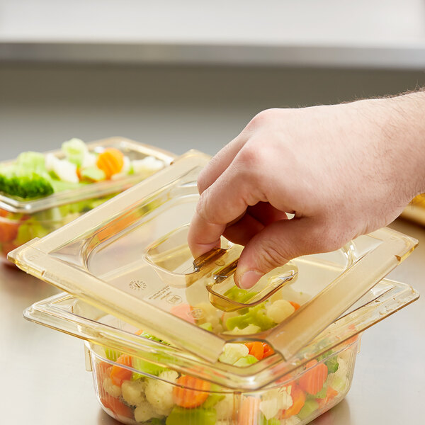 A hand using a Vollrath Super Pan slotted lid to serve food into a plastic container.