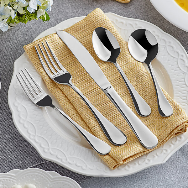 A five-piece set of Acopa Vittoria 18/8 stainless steel extra heavy weight flatware displayed on a folded beige napkin atop a white plate.