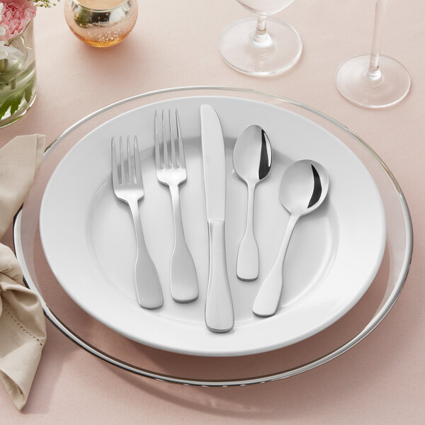 A five-piece set of stainless steel flatware, including two forks, a knife, and two spoons, displayed on a white plate.
